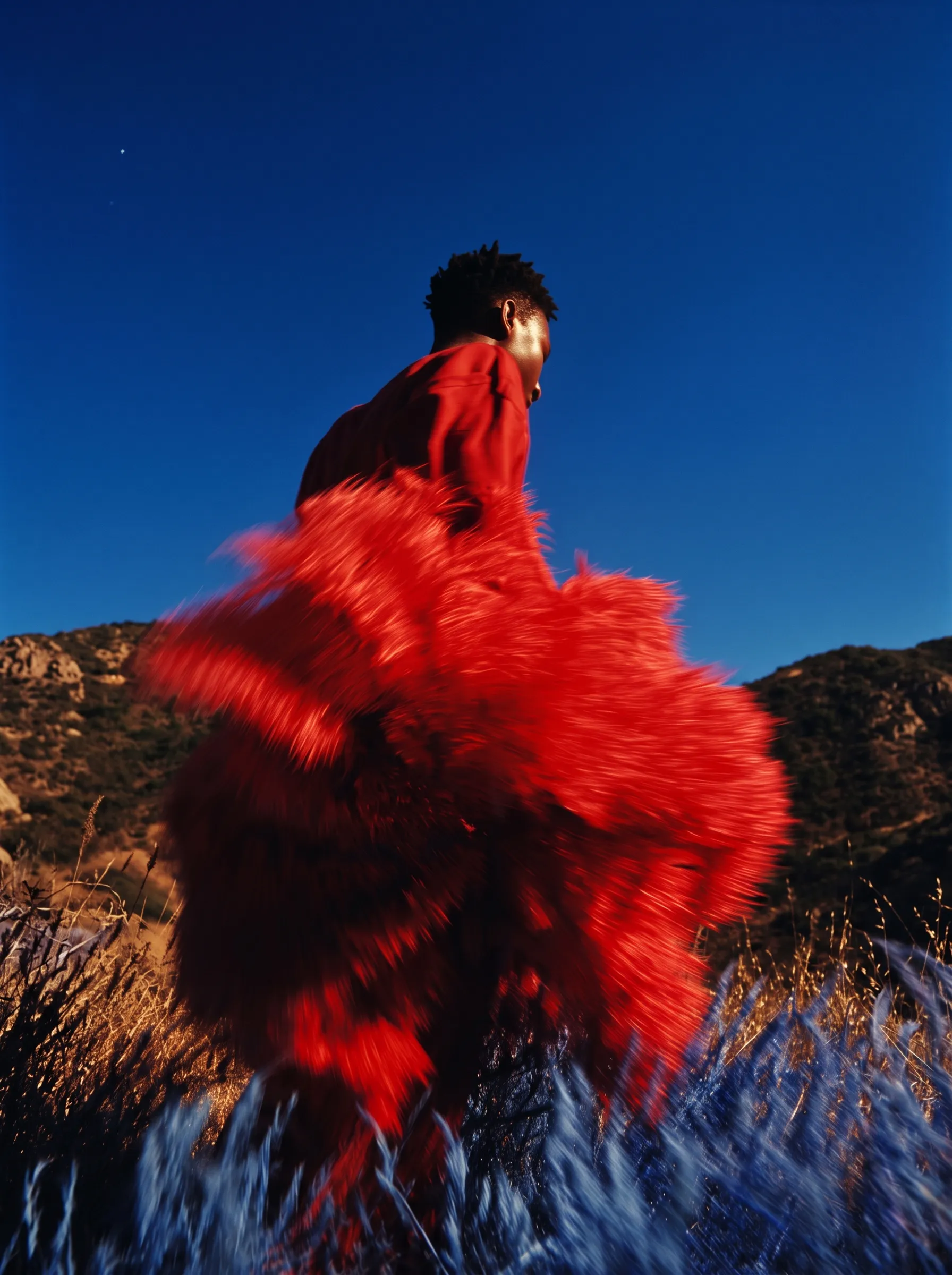 Mirage campaign featuring a model in a flowing red garment outdoors beneath a deep blue sky.
